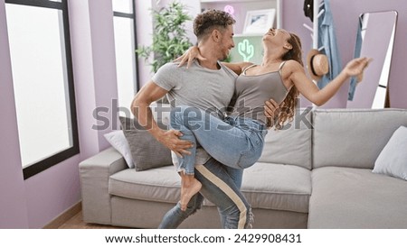 A joyful man lifting a laughing woman in a bright, modern living room, expressing love and happiness.