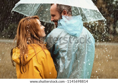 Joyful man strolling with woman in rain. They are looking at each other with content and love
