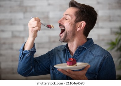 joyful man taking a mouthful of cake - Shutterstock ID 2110464590