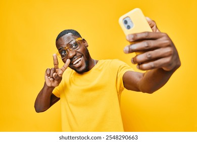 joyful man taking selfie, smiling, bright yellow background, casual outfit, emotion of happiness, engaged in social interaction, positive vibes, youth culture, lifestyle image - Powered by Shutterstock