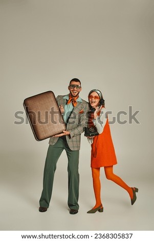 joyful man with vintage suitcase near woman talking on retro phone on grey, old-fashioned couple