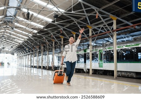 A joyful man waves enthusiastically while walking through a train station with a suitcase. Vibrant atmosphere captures the excitement of travel and new adventures.