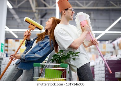 joyful married couple have fun in the market, young caucasian man and woman hold mops in hands, dance and sing - Powered by Shutterstock