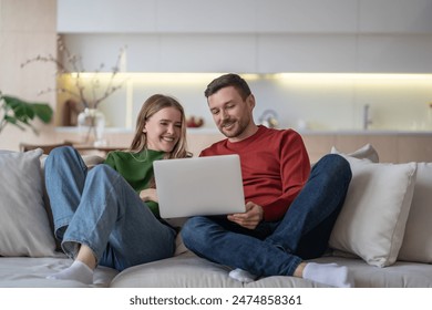 Joyful married couple watching fun movie using laptop, smiling sitting on comfortable couch in living room. Relaxed happy man and woman looking on screen computer laughing, enjoy lazy time together. - Powered by Shutterstock