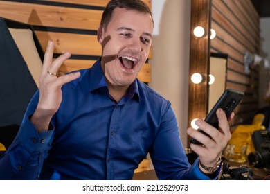 Joyful Mature Man In A Blue Shirt With His Hand Raised Looks At The Phone And Rejoices At The Good News In The Dressing Room