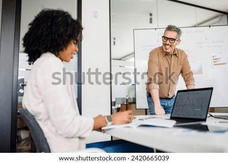 A joyful mature man, manager or mentor, explains concept to focused colleagues, demonstrating an engaging brainstorm session in a bright office setting, with emphasis on teamwork and knowledge sharing