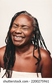 Joyful Mature Woman Laughing Cheerfully While Wrapped In A Bath Towel. Refreshed Woman With Dreadlocks Standing Against A White Background. Happy Middle Aged Woman Taking Care Of Her Ageing Body.