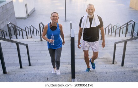 Joyful Middle Aged Couple, Man And Woman In Sportswear Smiling At Camera, Walking Up The Stairs After Working Out Together Outdoors