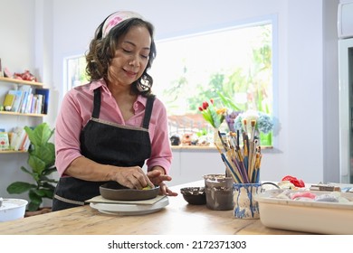 Joyful middle aged woman wearing apron making ceramic pot from clay in pottery workshop. Activity, handicraft, hobbies concept - Powered by Shutterstock