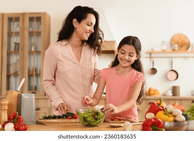 Joyful Middle Eastern Mother And Preteen Daughter Cooking Healthy Vegetable Salad For Dinner At Modern Kitchen Interior. Mom And Kid Girl Cutting Veggies Preparing Food Together. Family Nutrition - Powered by Shutterstock