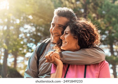 Joyful middle-aged couple embracing in a natural setting. The man and woman are smiling warmly, showcasing love and companionship. Sunlight filters through trees, creating a romantic atmosphere. - Powered by Shutterstock