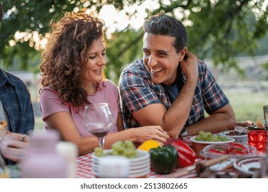 Joyful middle-aged couple sharing intimate moment at outdoor dinner party. Romantic picnic scene with wine and fresh produce. Love, relationships, and enjoying life together in natural setting. - Powered by Shutterstock