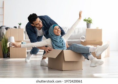 Joyful middle-eastern young family having fun while unpacking stuff in their new house. Happy arab guy and excited lady in hijab sitting in paper box, enjoying moving. Apartment, house, real estate - Powered by Shutterstock