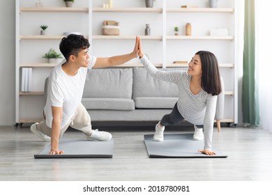 Joyful Millennial Asian Man And Woman In Sportswear Cheering Up Each Other While Planking At Home, Giving High Five And Smiling, Doing Exercises On Fitness Mats At Living Room, Healthy Lifestyle