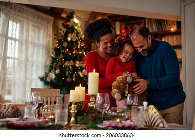 Joyful Mixed Race Family Celebrating Christmas Party At Home, Smiling, Having Fun And Enjoying Themselves With The Teddy Bear.