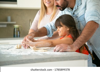 Joyful Mom And Dad Teaching Happy Daughter To Roll Dough On Kitchen Table With Flour Messy. Young Couple And Their Girl Baking Buns Or Pies Together. Family Cooking Concept