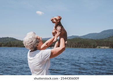 Joyful moment between an elderly woman and her small dog by a peaceful lakeside natural adding to the sense of peace and relaxation holidays concept. - Powered by Shutterstock