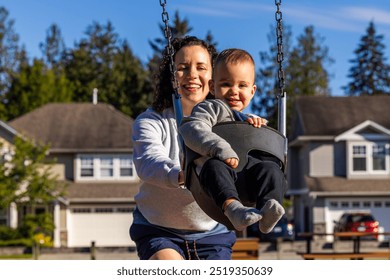 Joyful moment of a mother and her smiling child on a swing in a sunny neighborhood park in Mission, BC. Captures family bonding and happiness outdoors. - Powered by Shutterstock