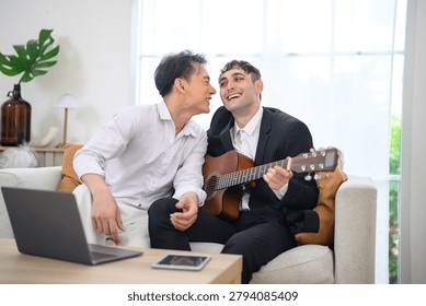A joyful moment shared between two men as one plays the guitar and the other listens, creating a warm and intimate atmosphere in their home