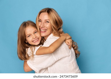 Joyful mother and daughter embracing with smiles on a vibrant blue background, expressing love and happiness together - Powered by Shutterstock