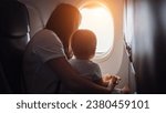 Joyful mother shows view from plane window to toddler girl. Child cradled in arms of mother as family embarks on memorable vacation together, sunlight