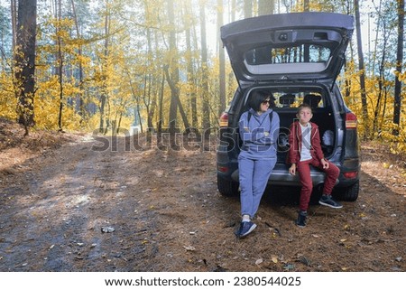 Joyful mother and son seated in an open car trunk in a sunny autumn forest, a family getaway in nature.