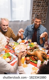 Joyful Multicultural Family Holding Hands During Dinner On Thanksgiving Holiday