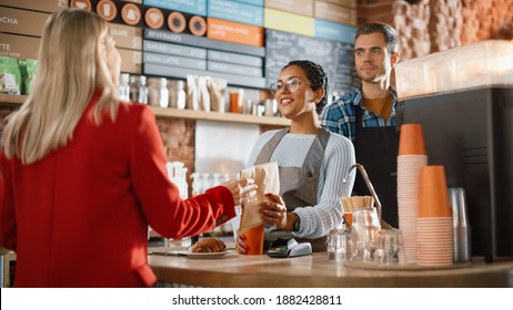 Joyful Multiethnic Diverse Woman Gives a Payment Terminal to Customer Using NFC Technology on Smartphone. Customer Uses Mobile to Pay for Take Away Latte and Pastry to a Barista in Coffee Shop. - Powered by Shutterstock