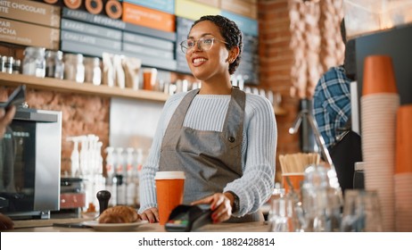 Joyful Multiethnic Diverse Woman Gives a Payment Terminal to Customer Using NFC Technology on Smartphone. Customer Uses Mobile to Pay for Take Away Latte and Pastry to a Barista in Coffee Shop. - Powered by Shutterstock