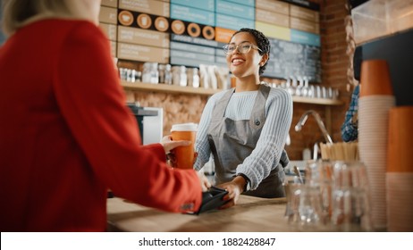 Joyful Multiethnic Diverse Woman Gives a Payment Terminal to Customer Using NFC Technology on Smartphone. Customer Uses Mobile to Pay for Take Away Latte and Croissant to a Barista in Coffee Shop. - Powered by Shutterstock