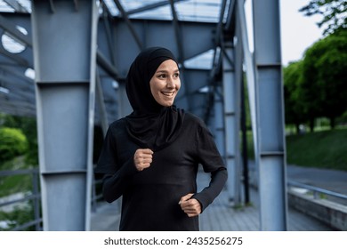 A joyful Muslim woman wearing a hijab enjoys a run in an urban park setting, exuding health and happiness. - Powered by Shutterstock