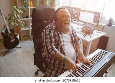 Joyful Obese Man Artist Plays Music On Synthesizer Near Table With Computer Monitors In Studio