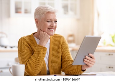 Joyful old grey-haired woman drinking coffee and using digital tablet in kitchen, empty space. Happy grandmother reading culinary blog or book online, surfing on Internet on modern pad at home - Powered by Shutterstock