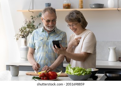 Joyful old senior woman showing online recipe on smartphone to smiling elderly retired husband, cooking healthy food together in modern kitchen. modern technology in everyday life of older people. - Powered by Shutterstock