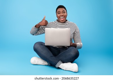 Joyful Overweight Black Woman Using Laptop Gesturing Thumbs Up Smiling To Camera Sitting On Blue Background. Female Freelancer Approving Website With Like Gesture Browsing Internet On Computer