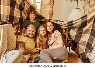 joyful parents and kids laughing under blanket hut in living room, playing together at home - Powered by Shutterstock