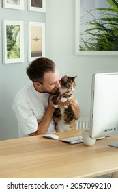 Joyful Pet Owner Man Playing With Cute Domestic Cat At Workplace Having Stress Relief From Problems At Work. Freelancer, Programmer Or Web Designer Sitting At Desk With Modern Computer In Home Office