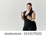 A joyful plus size woman holds a water bottle and checks her phone, exuding elegance and confidence.