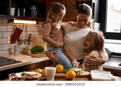  A joyful portrait in the kitchen: a mother and her two daughters, smiling and hugging, pose for a heartwarming photo.