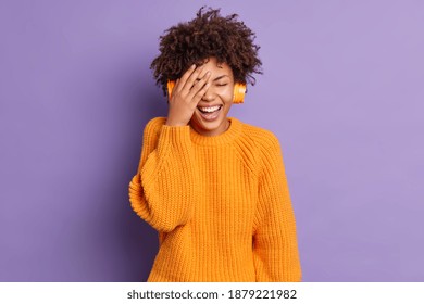 Joyful positive young African American woman makes face palm wears stereo wireless headphones listens audio track poses against vivid purple background. People happy emotions and leisure concept - Powered by Shutterstock