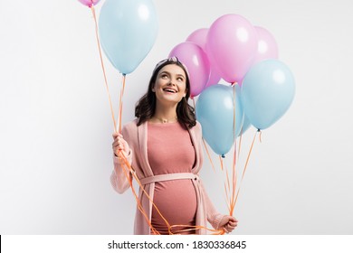 joyful and pregnant woman in dress holding balloons and looking up isolated on white