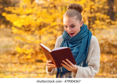 Joyful pretty female enjoying a great book in the forest full of leaves