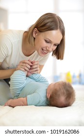 Joyful Pretty Woman Holding Baby Feet. Mom Looks Tenderly At Small Son.