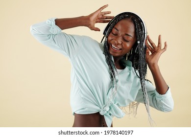 Joyful pretty young woman dancing and singing when lstening to music in headphones, isolated on yellow