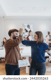 Joyful professional interaction captured as two colleagues high-five in a well-lit office setting, symbolizing team success, support, and positive workplace culture, with other people in the