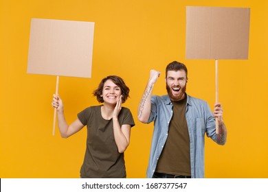 Joyful protesting two people guy girl hold protest signs broadsheet blank placard on stick doing winner gesture isolated on yellow background. Protests strikes pickets concept. Youth against city
