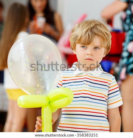 joyful or sad kid boy on birthday party with an air balloon, indoors. Animators on background.
