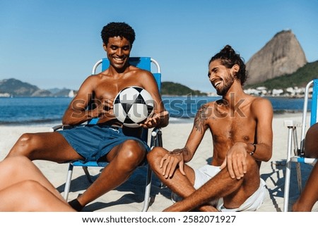 A joyful scene of two friends sharing laughter while relaxing at the beach with a soccer ball. The iconic Sugarloaf Mountain is visible in the background, highlighting a perfect day at the beach.