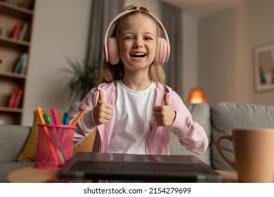 Joyful Schoolgirl Showing Like To Laptop, Gesturing Thumbs Up Smiling To Camera Learning Online Sitting At Desk At Home, Wearing Earphones. I Like E-Learning. Selective Focus