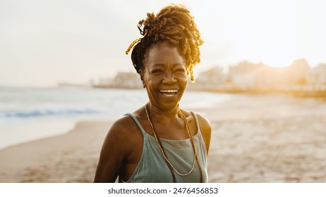 Joyful senior African American woman with braids enjoying a beautiful sunset at the beach, exuding happiness and confidence. - Powered by Shutterstock